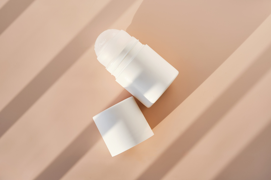 Weißer Deo-Roller mit abgenommener Kappe auf beiger Fläche im Sonnenlicht