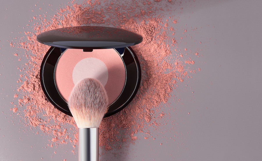 Geöffnete Puderdose mit pfirsichfarbenem Rouge, Make-up-Pinsel und verstreutem Puder
