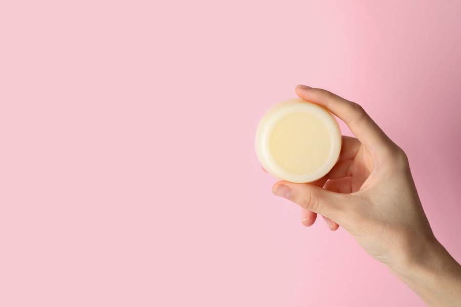 Hand hält ein rundes festes Shampoo vor rosa Hintergrund