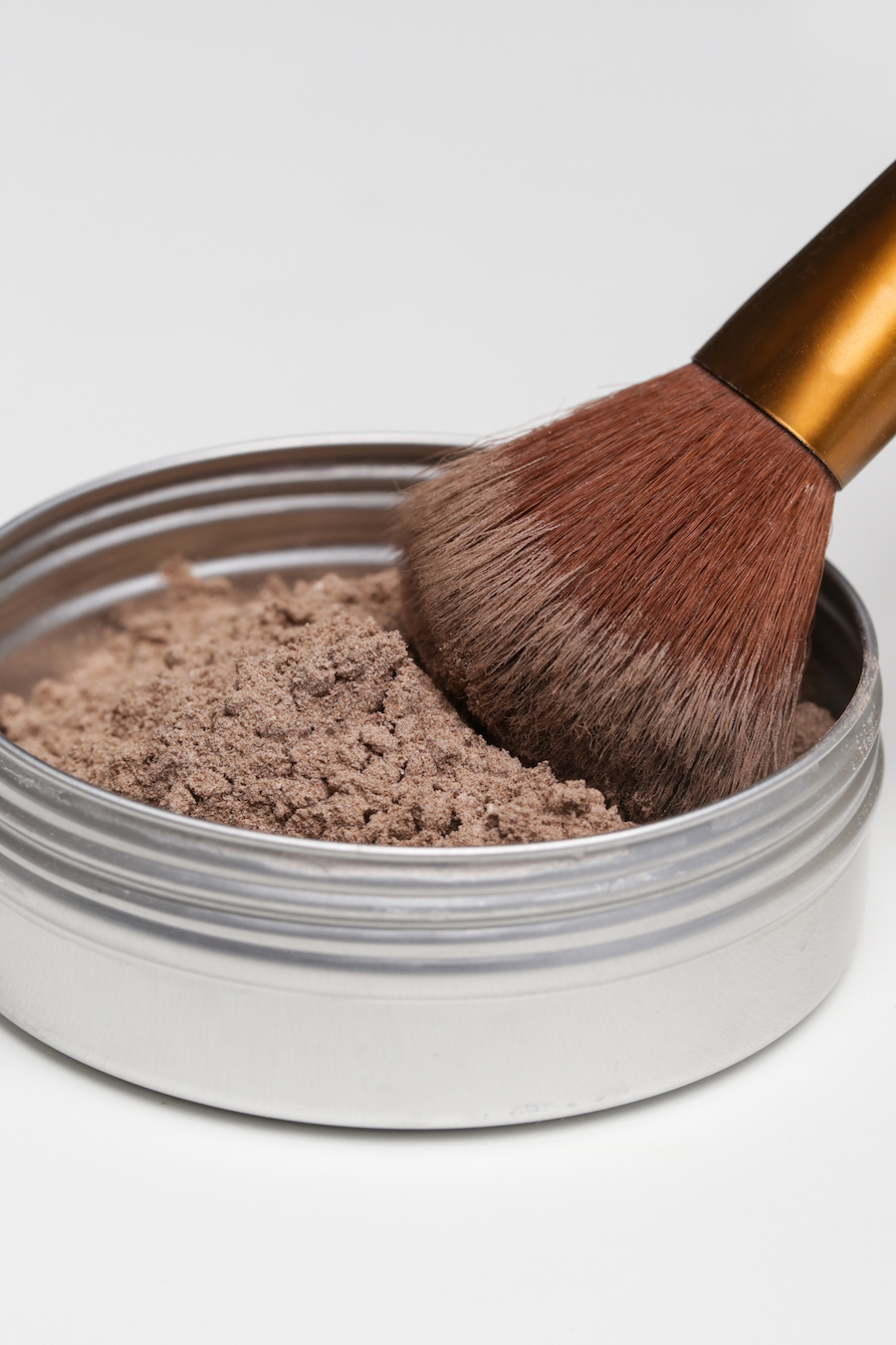 Make-up-Pinsel nimmt hellbraunes loses Puder aus einer Metalldose auf