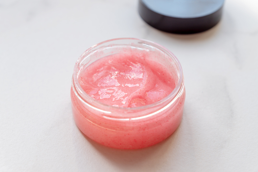 Offener Tiegel mit rosa Peelingcreme und feinen Peelingpartikeln auf Marmor