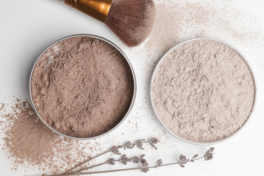 Zwei Dosen getöntes Puder in Dunkel- und Hellbraun mit Make-up-Pinsel und Lavendelzweigen