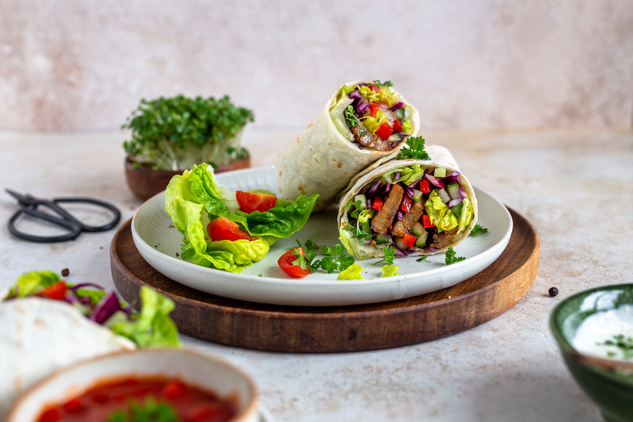 Zwei Hälften eines Wraps mit pflanzlichen Streifen, Salat, Tomate und Rotkraut auf einem Teller