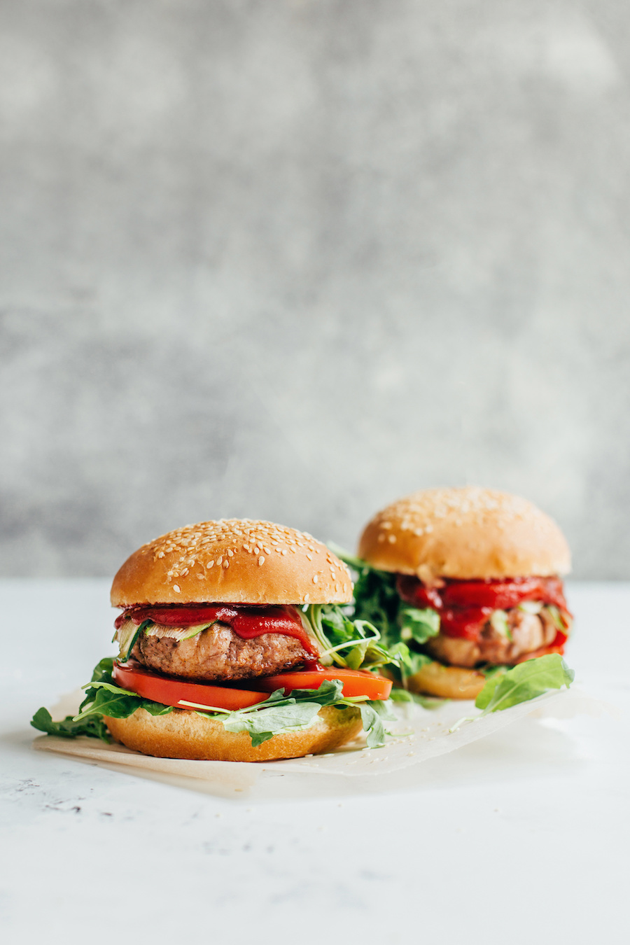 Zwei Burger mit pflanzlichen Patties, Tomate, Rucola und Sauce in Sesambrötchen