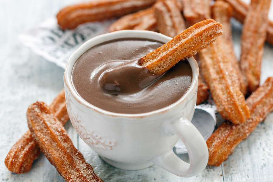 Tasse mit dickflüssiger Schokoladen-Dessertcreme, gezuckerte Churros zum Eintunken daneben