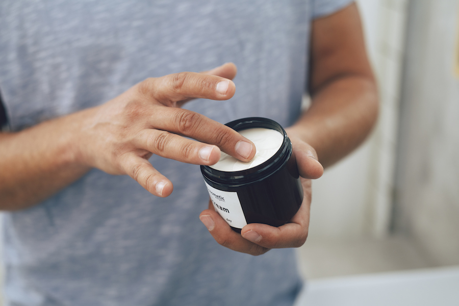 Mann nimmt mit dem Finger Creme aus einem offenen schwarzen Tiegel