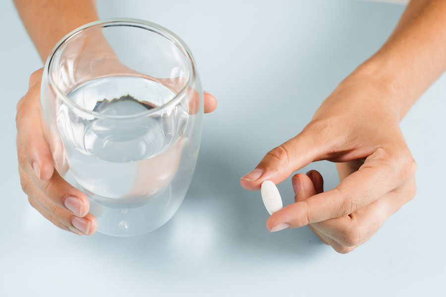 Hände halten ein Glas Wasser und eine weiße längliche Tablette
