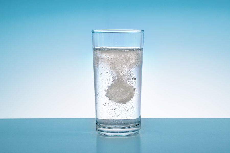 Brausetablette löst sich in einem Glas Wasser auf blauem Hintergrund auf
