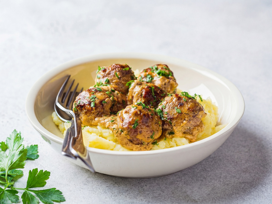 Schale mit Fleischbällchen in Rahmsauce auf Kartoffelpüree mit Petersilie und Gabel