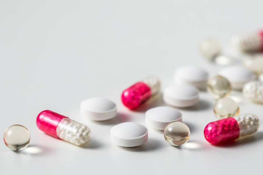 Weiße Tabletten, rosa Kapseln und durchsichtige Weichkapseln auf weißer Fläche