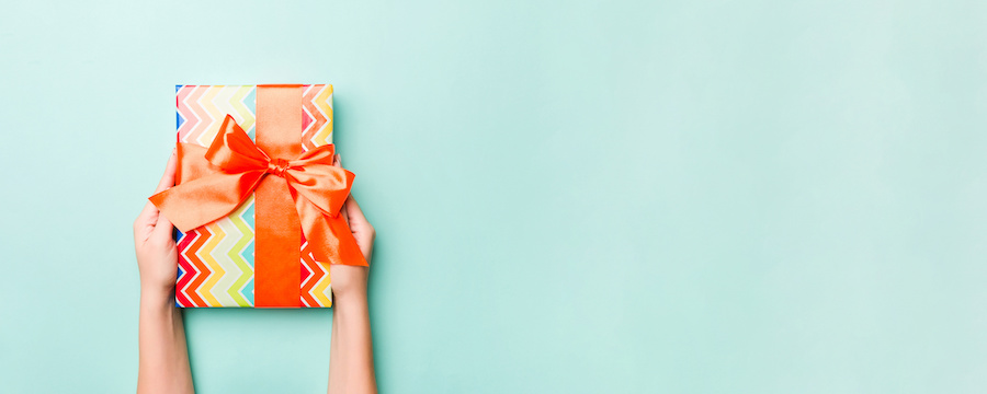 Hände halten ein Geschenk in buntem Zickzack-Papier mit orangefarbener Schleife