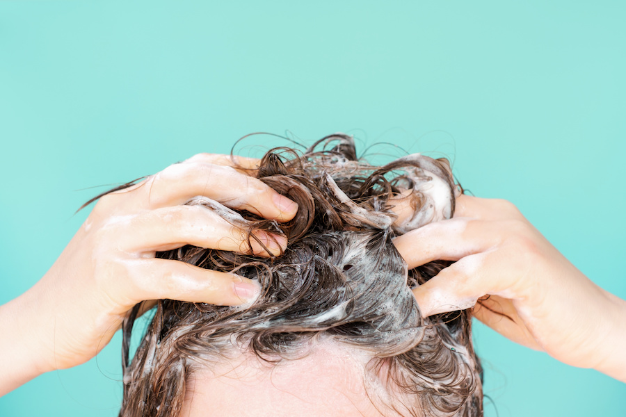 Hände massieren Shampoo-Schaum in braunes Haar vor türkisem Hintergrund