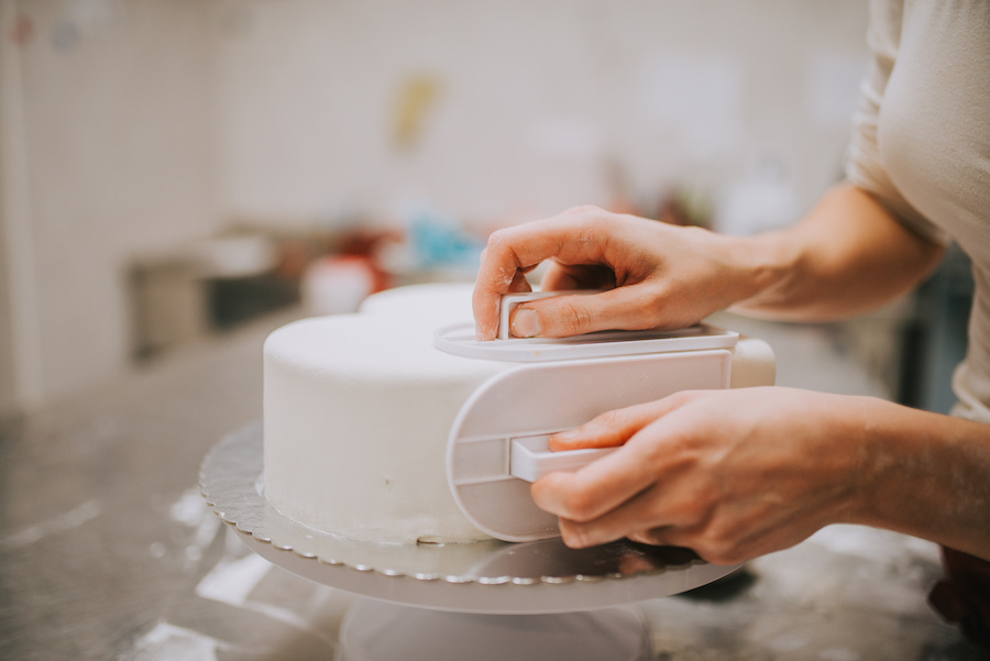 Hände glätten weißes Fondant auf einer runden Torte mit einem Glätter