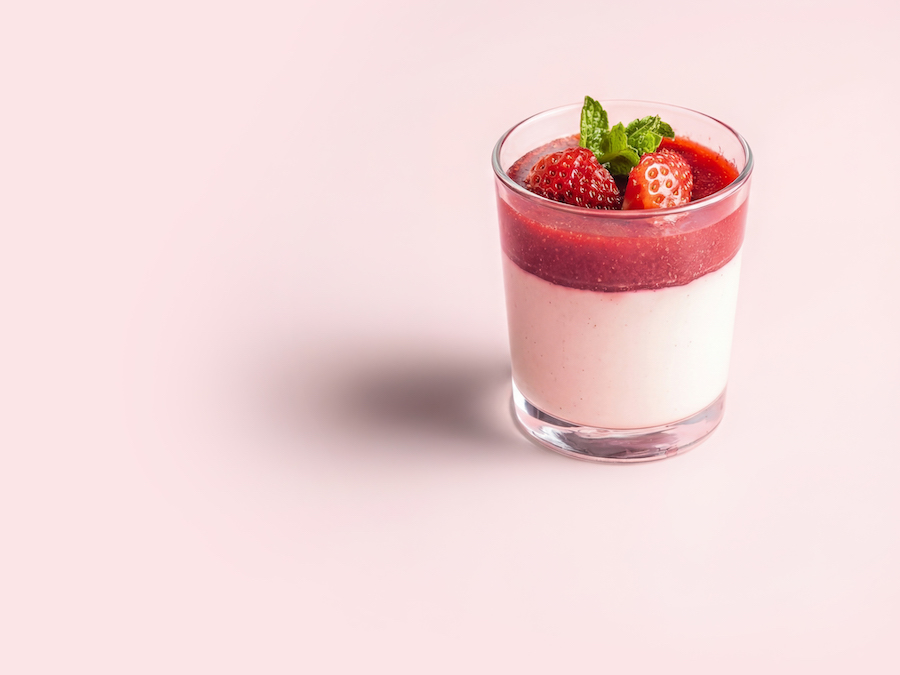 Panna cotta im Glas mit Erdbeersauce und frischen Erdbeeren auf rosa Hintergrund