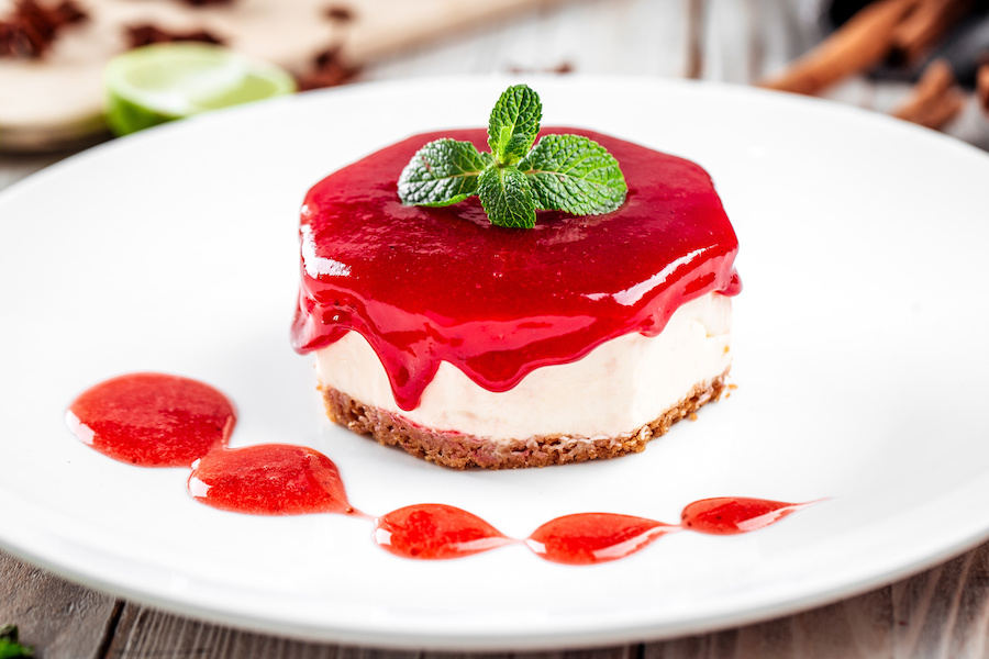 Käsekuchen mit Erdbeer-Fruchtaufstrich und Minzblättern auf einem weißen Teller