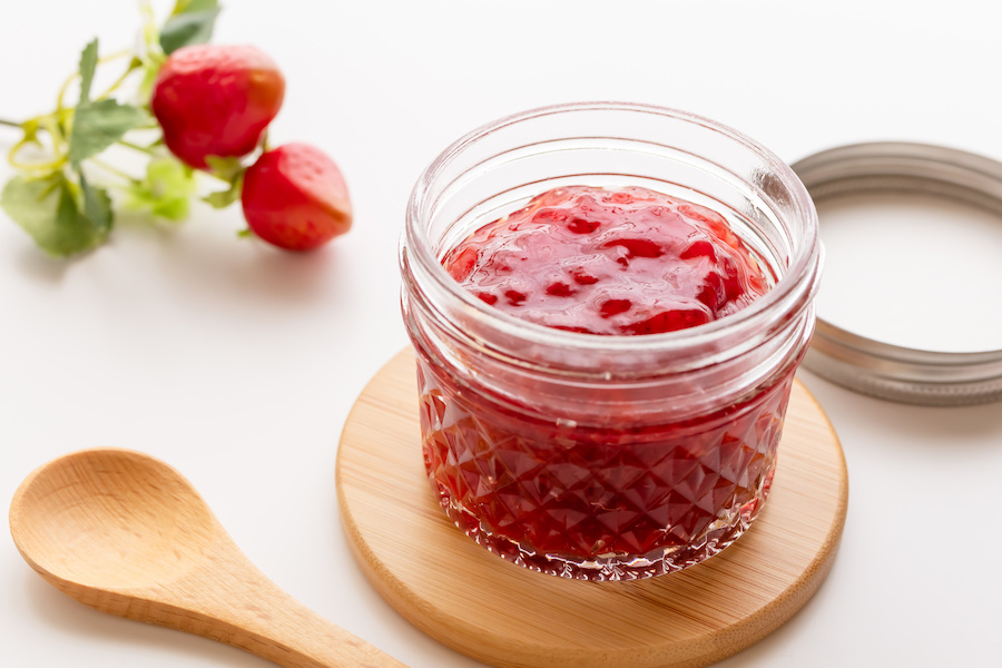 Offenes Glas Erdbeermarmelade auf einem Holzbrett mit frischen Erdbeeren und Holzlöffel