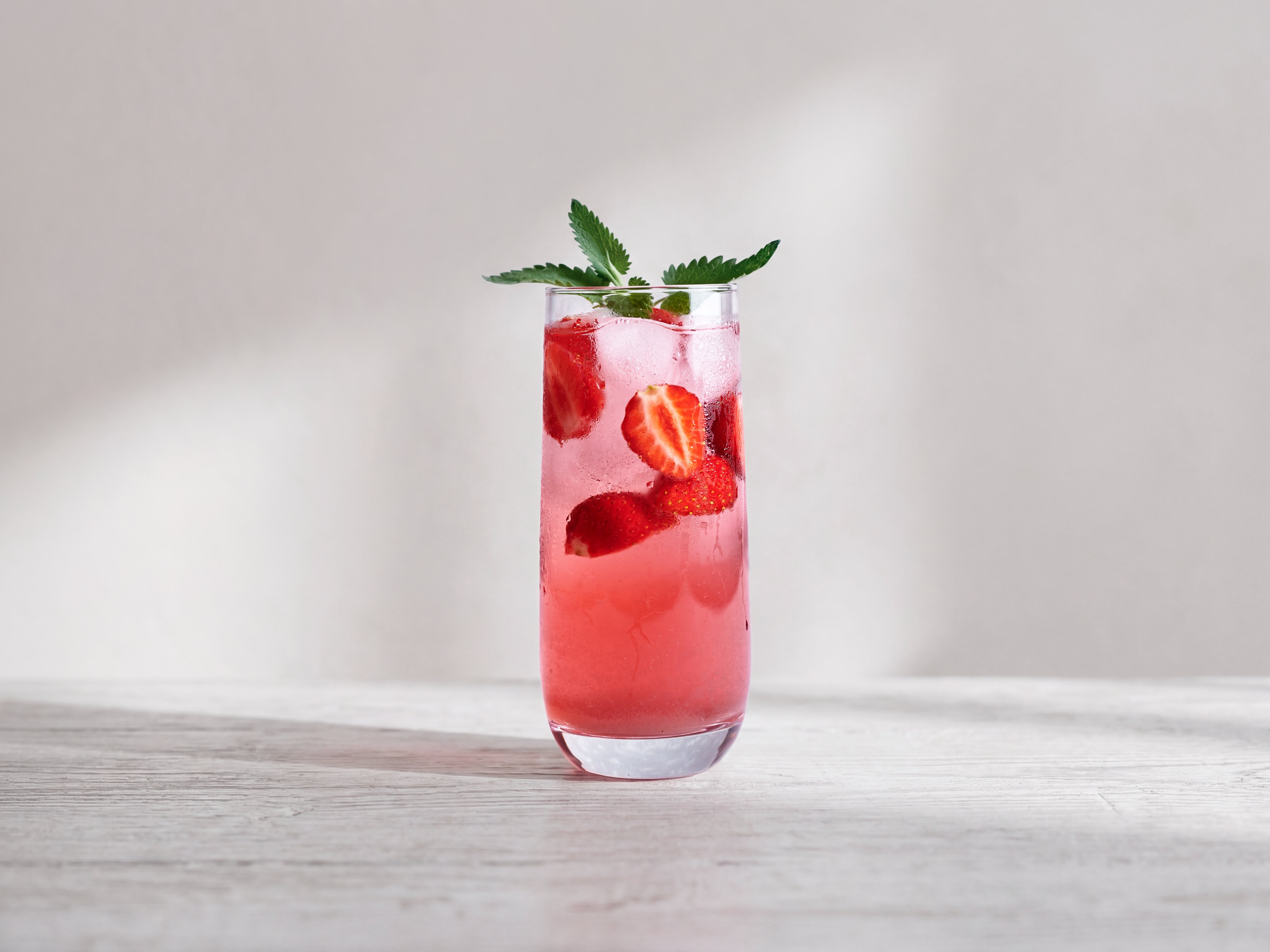 Hohes Glas mit Erdbeersirup-Drink, Erdbeerstücken, Eis und Minze