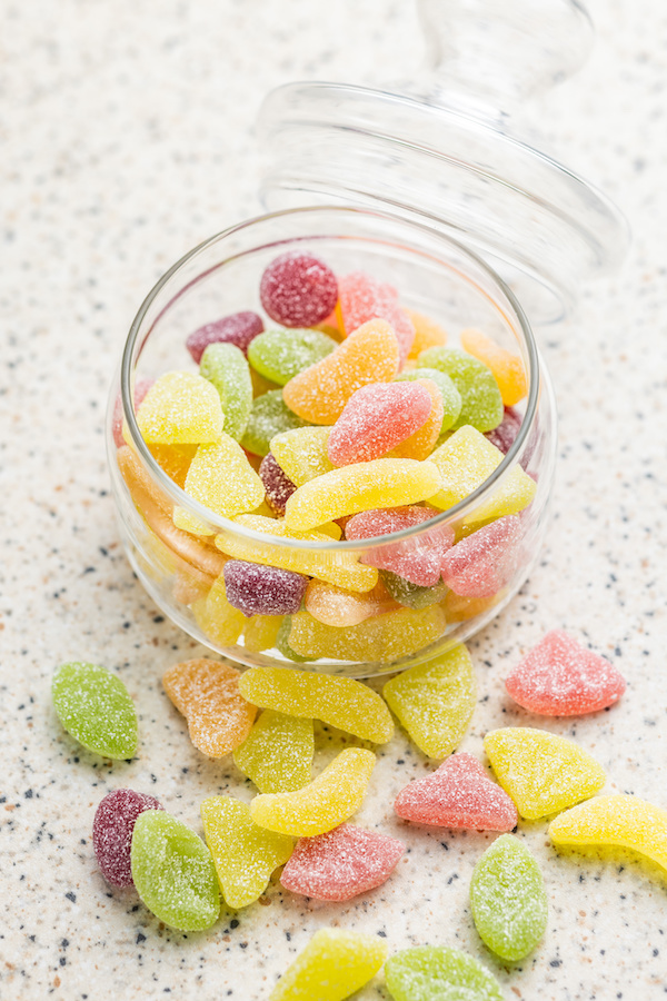 Glasdose mit zuckrigen Fruchtgummis in Gelb, Grün, Orange und Rot auf einer gesprenkelten Arbeitsfläche