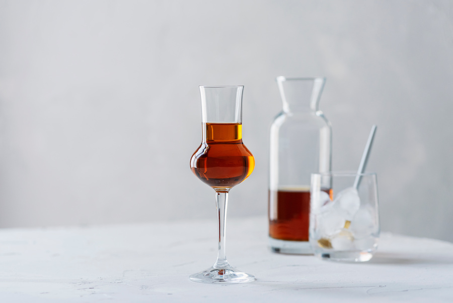 Stemmed glass of amber liqueur with a carafe and a tumbler of ice behind it