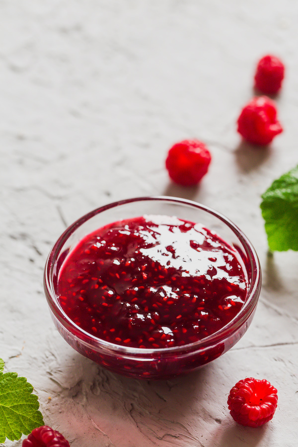 Glass bowl of raspberry fruit preparation with fresh raspberries and mint leaves
