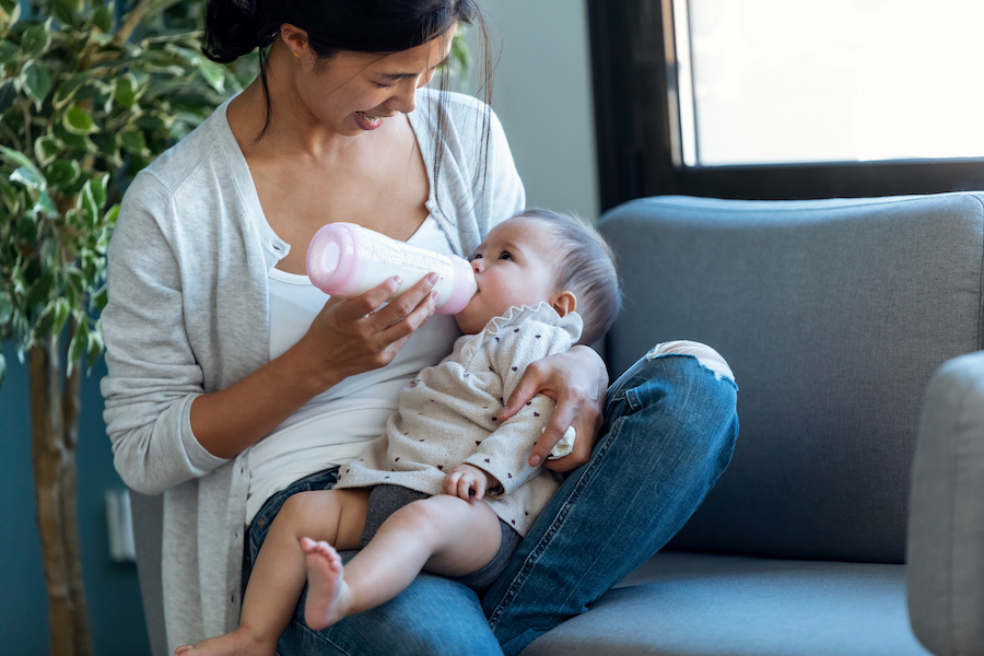 Lächelnde Mutter füttert ihr Baby mit dem Fläschchen in einem Sessel