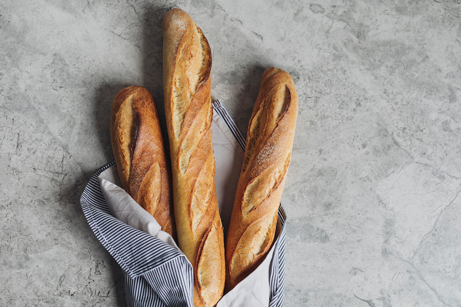 Drei knusprige Baguettes in einem gestreiften Tuch auf grauer Steinfläche