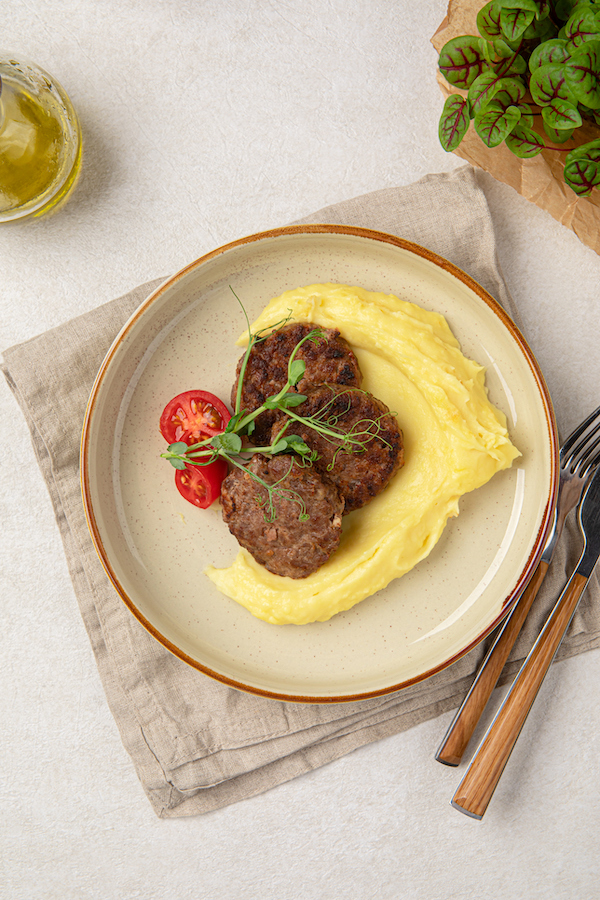 Drei Fleischlaibchen mit Kartoffelpüree, Tomate und Erbsensprossen auf einem Teller