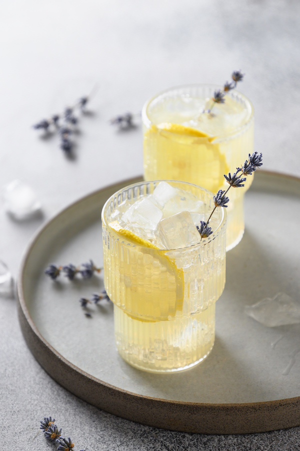 Zwei Gläser Limonade mit Eis, Zitronenscheiben und Lavendelzweigen auf einem Keramiktablett