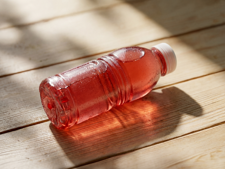 Plastikflasche mit rosa Vitaminwasser auf sonnenbeschienenen Holzbrettern