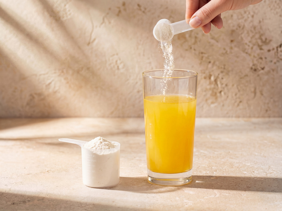 Proteinpulver wird aus einem Messlöffel in ein Glas mit orangefarbenem Getränk geschüttet