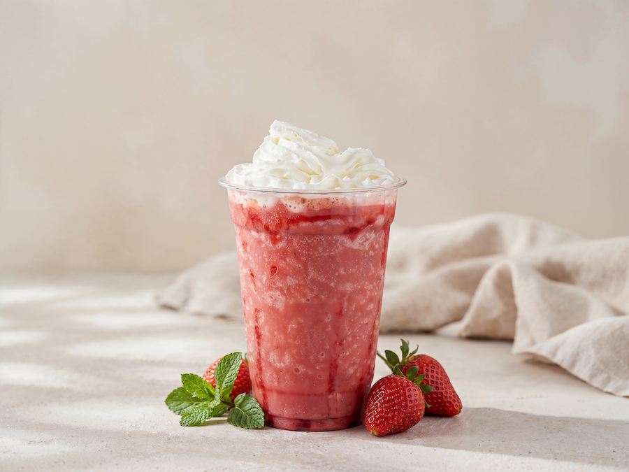 Strawberry frappé in a plastic cup topped with whipped cream, fresh strawberries and mint
