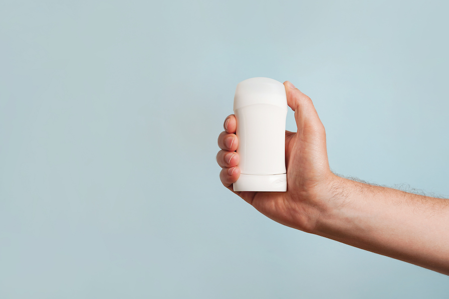Hand holding a white deodorant stick against a light blue background