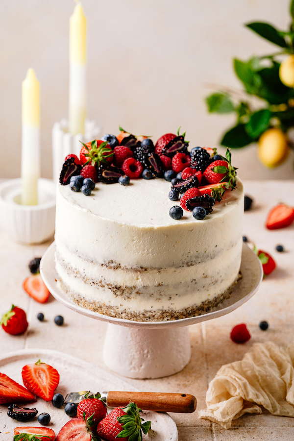 Semi-Naked-Torte mit Cremeglasur und frischen Beeren auf einer Tortenplatte mit Kerzen