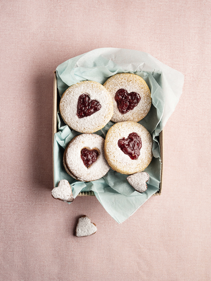 Jam-filled shortbread cookies with heart-shaped cut-outs and powdered sugar in a gift box