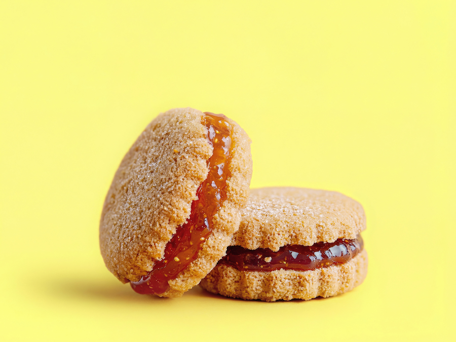Zwei mit Zucker bestäubte Doppelkekse mit roter Fruchtmarmeladenfüllung vor gelbem Hintergrund