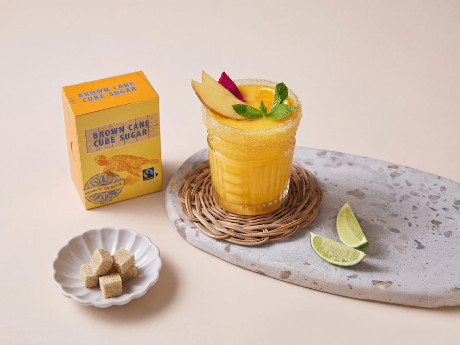 Mango-Smoothie mit Zuckerrand neben einer Packung Brown Cane Cube Sugar und einer Schale brauner Würfelzucker