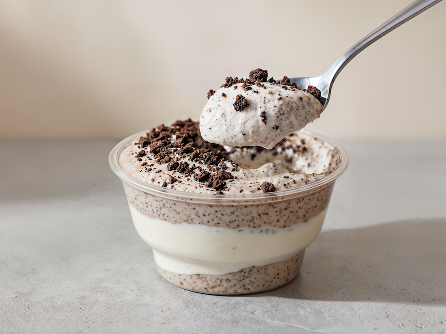 Layered cookies-and-cream dessert in a cup with a spoonful lifted, cookie crumbs on top