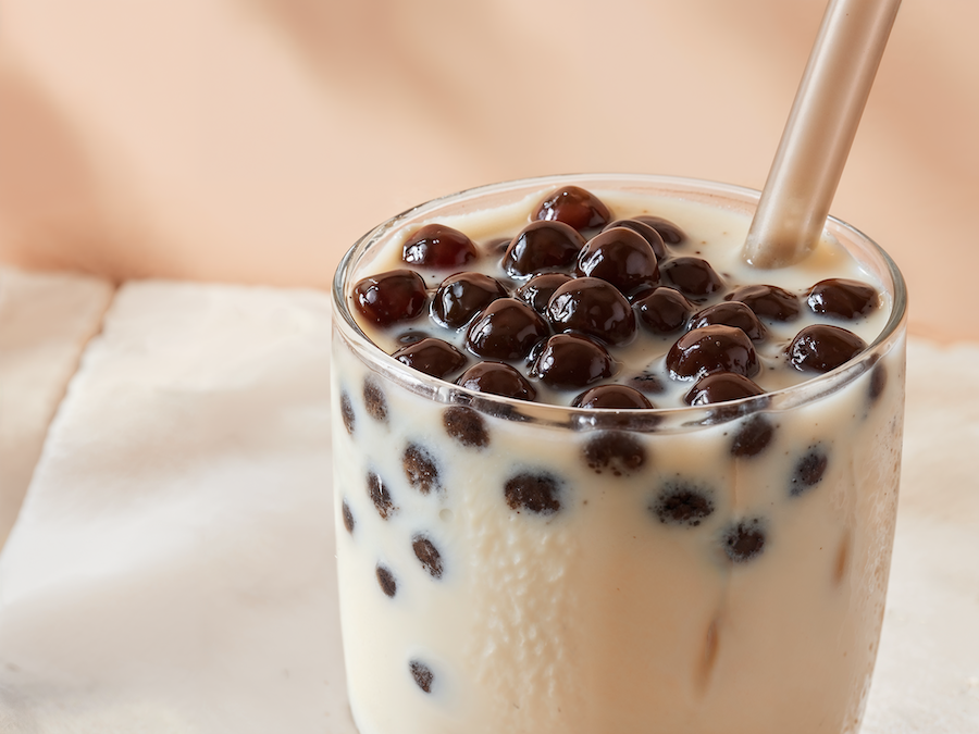 Glass of milky bubble tea with dark tapioca pearls and a straw