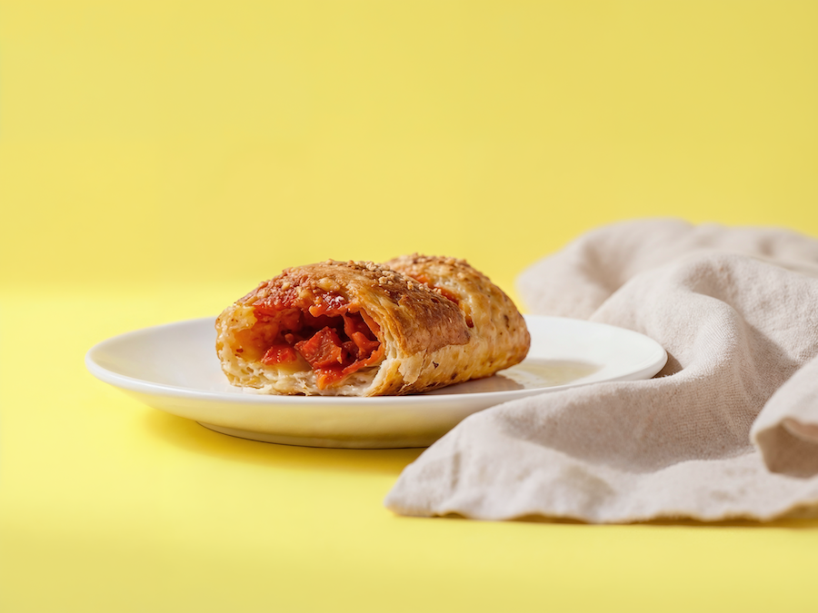 Blätterteigtasche mit Tomatenfüllung auf einem weißen Teller vor gelbem Hintergrund