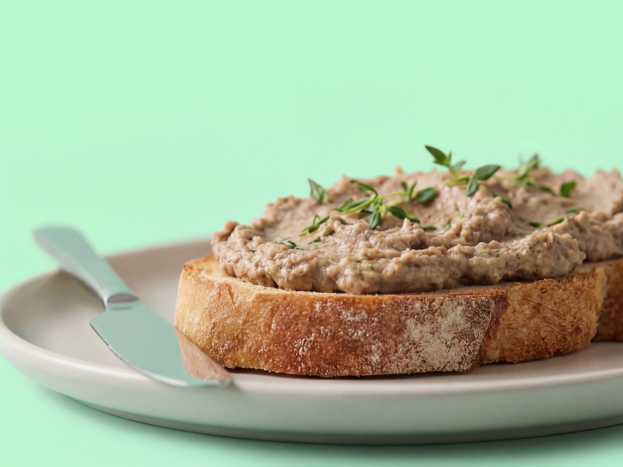 Slice of bread topped with a savory spread and fresh thyme on a plate, mint green background