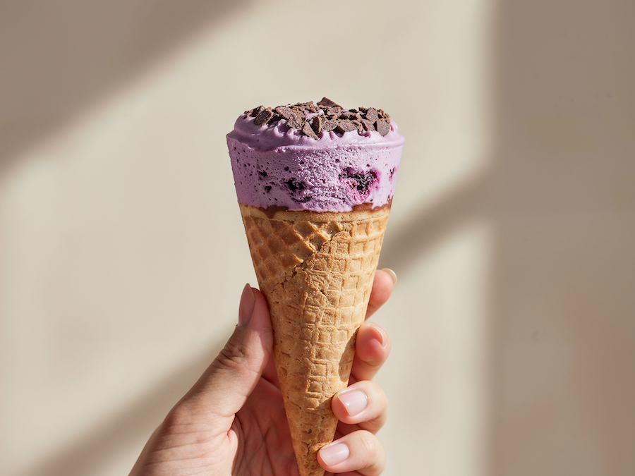 Hand hält eine Waffeltüte mit violettem Beereneis und Schokoladenstückchen