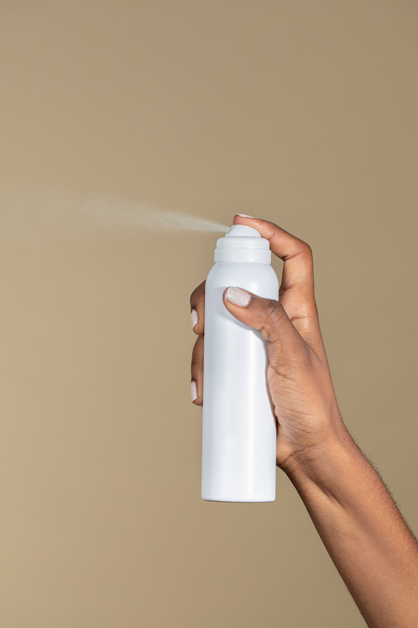 Hand spraying a white aerosol can against a beige background