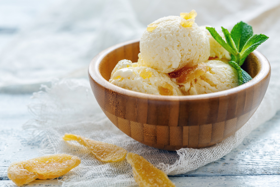 Wooden bowl of vanilla ice cream with candied ginger pieces and mint