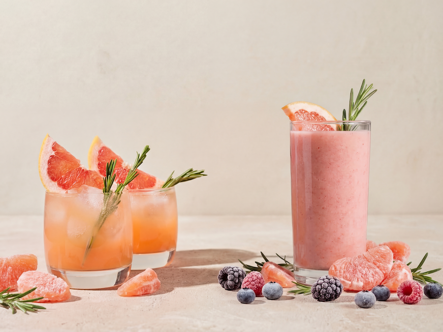 Two grapefruit drinks with rosemary and a pink smoothie next to citrus segments and berries