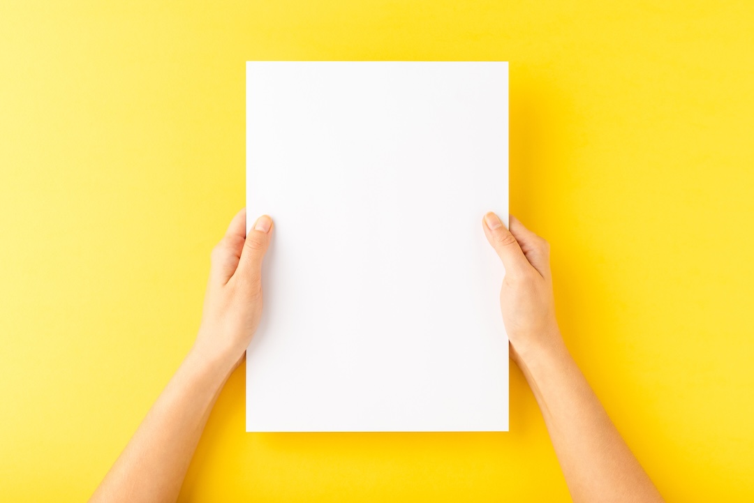 Zwei Hände halten ein leeres weißes Blatt Papier vor gelbem Hintergrund