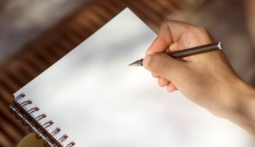 Hand schreibt mit einem Stift in ein leeres Spiralnotizbuch