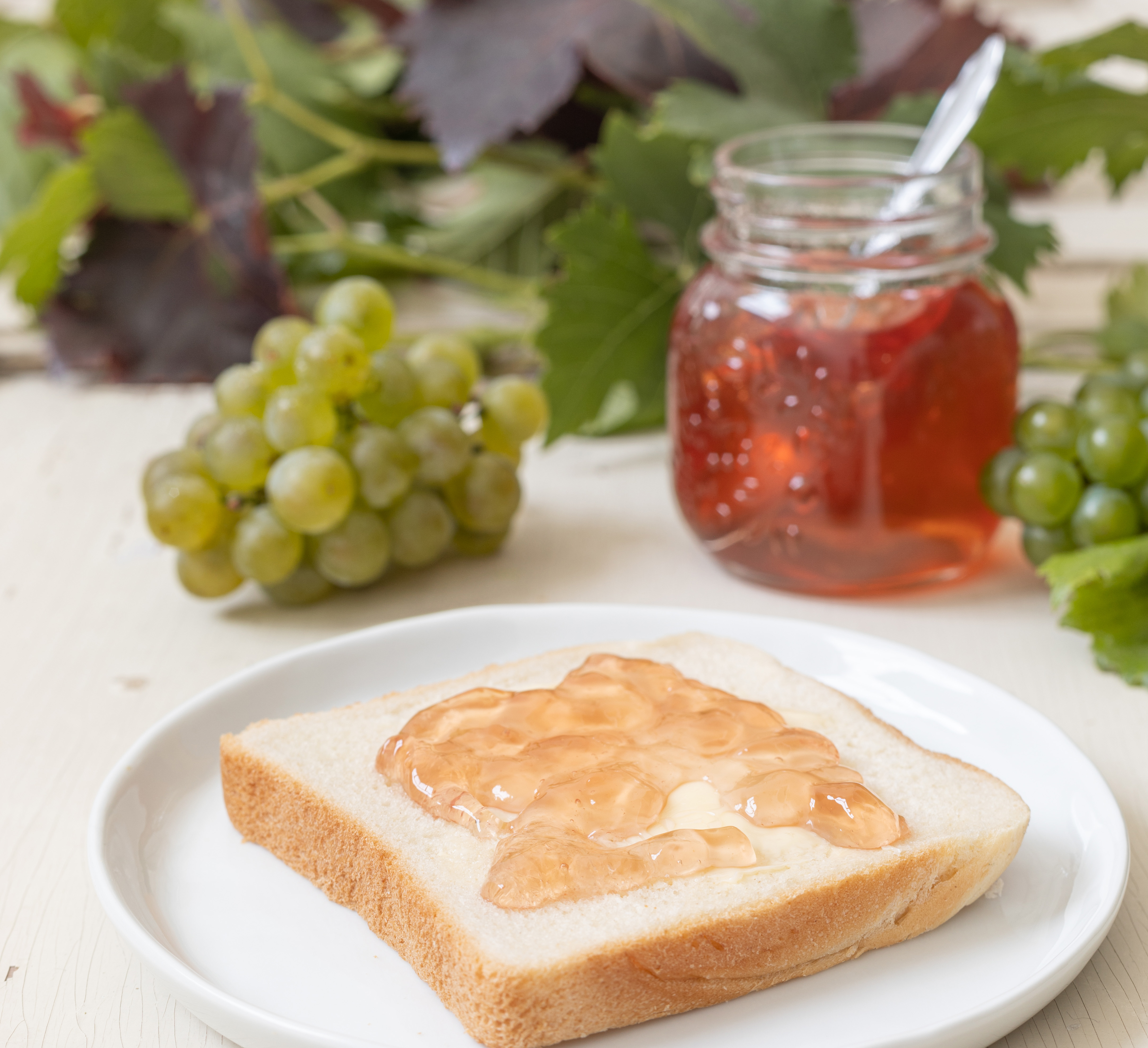 Toastscheibe mit Traubengelee, ein Glas Gelee und frische grüne Trauben mit Weinblättern