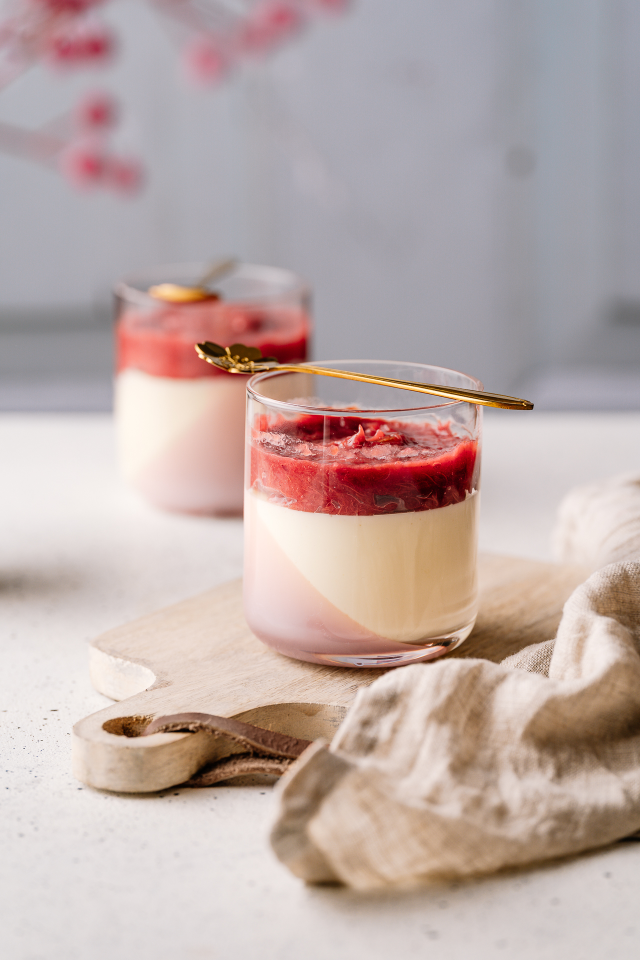 Two glasses of panna cotta topped with strawberry compote on a wooden board
