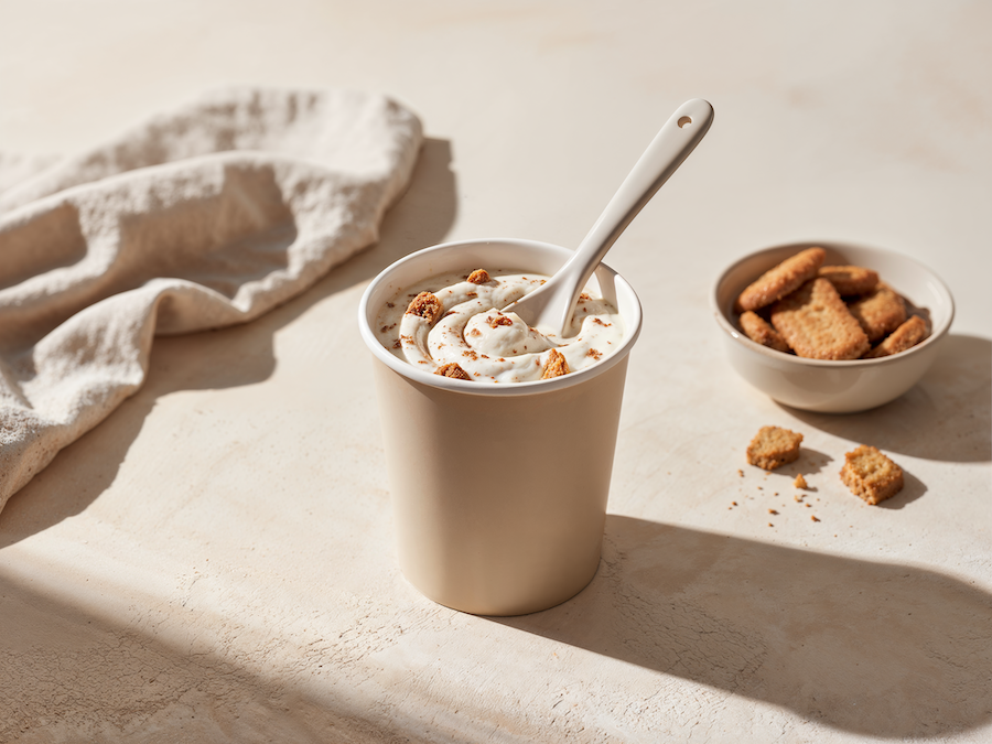 Paper cup of creamy dip with crunchy inclusions and a spoon, next to a bowl of crackers