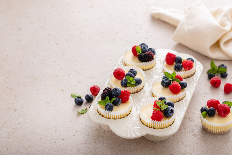 Mini-Cheesecakes mit Heidelbeeren, Himbeeren und Minze in einer weißen Muffinform